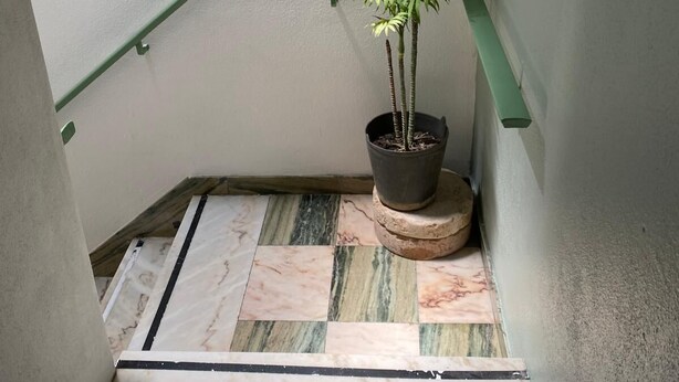 Eine Treppe mit grüner Handlauf, einem Blumentopf und einem Marmorboden.