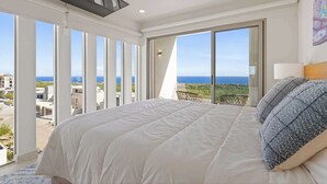 Une chambre dotée d’un grand lit, offrant une vue sur la mer et comprenant un balcon aménagé avec du mobilier d’extérieur.