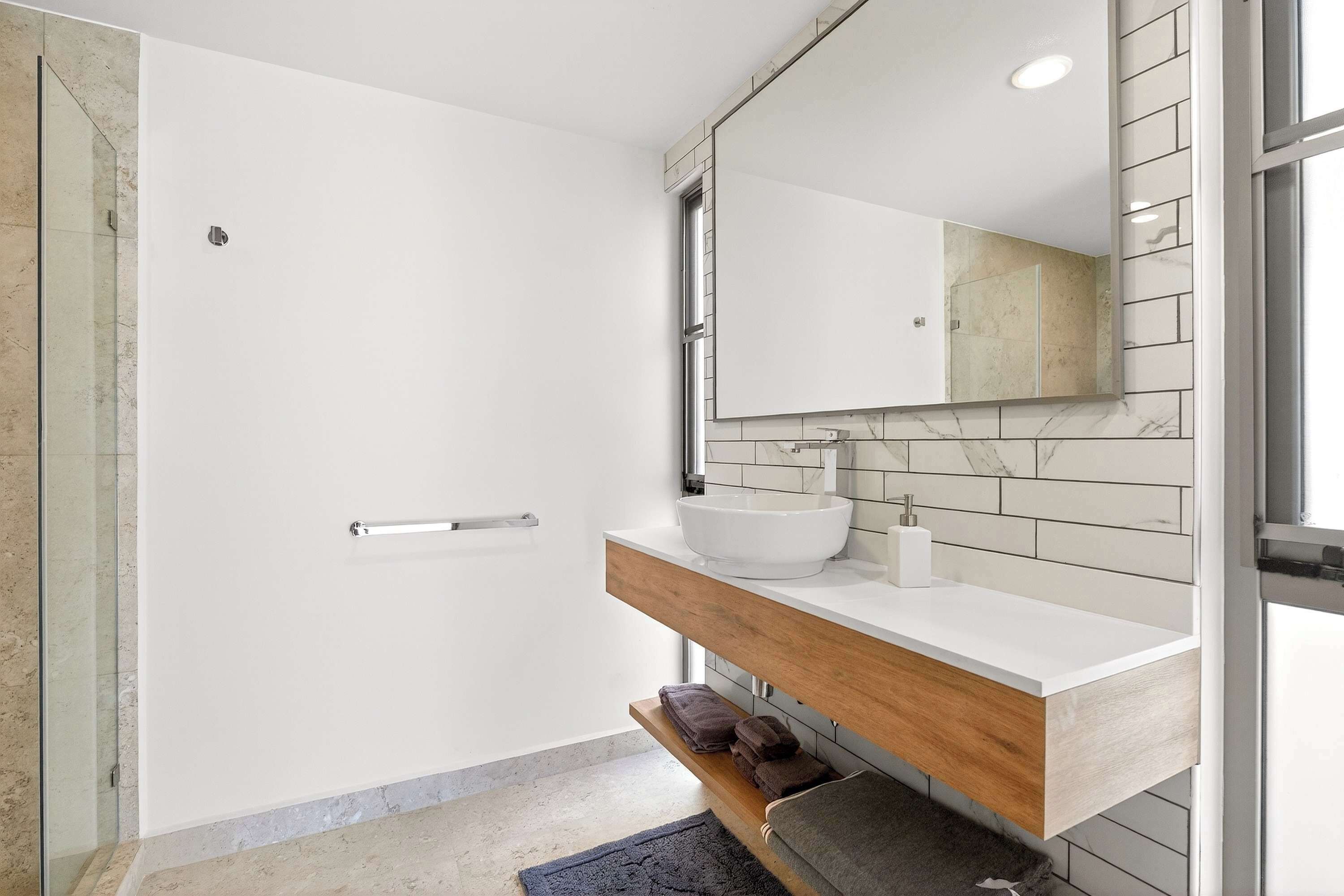 A modern bathroom with a glass shower enclosure, a white sink with a marble countertop, and a wooden vanity with a mirror.