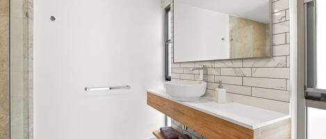 A modern bathroom with a glass shower enclosure, a white sink with a marble countertop, and a wooden vanity with a mirror.