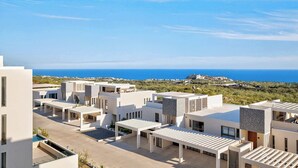 Un complexe résidentiel moderne composé de plusieurs bâtiments, doté d’une piscine et offrant une vue sur la mer.