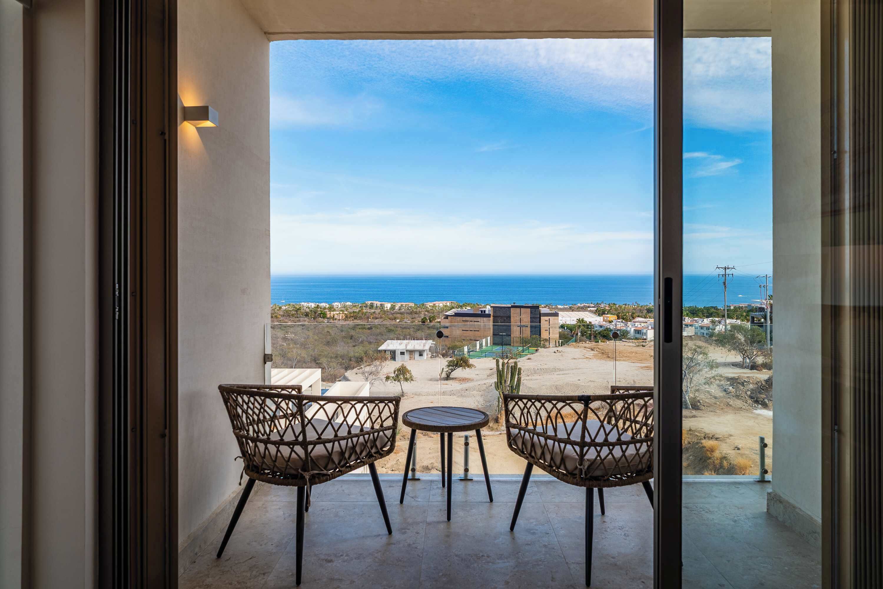 Un balcon avec deux fauteuils en osier et une petite table, offrant une vue sur la côte, avec des bâtiments et un ciel dégagé.