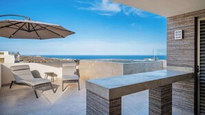 Une terrasse extérieure moderne avec vue sur la mer, comprenant une table, des chaises et un parasol.