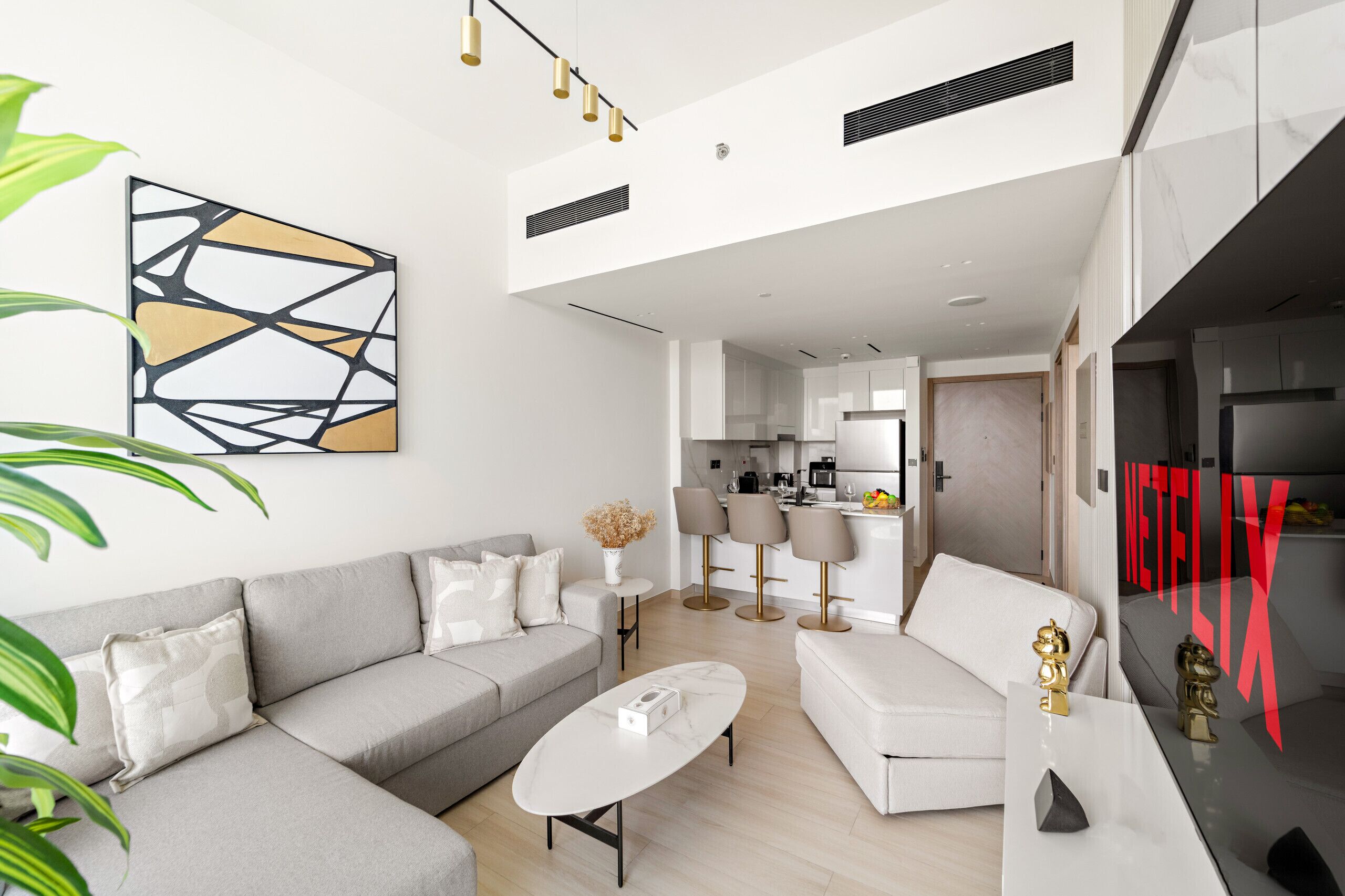 A modern living room with a grey sofa, a white coffee table, and a kitchen in the background.