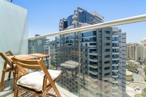 A balcony with a glass railing, wooden chairs, and a table. - Modern Studio with Beach Access, Palm Jumeirah (Dubai)