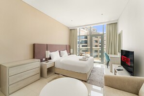 A modern hotel room with a large bed, a TV, a desk, and a view of the city. - Modern Studio with Beach Access, Palm Jumeirah (Dubai)