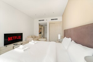 A hotel room with a large bed, a TV displaying 'NETFLIX', a sofa, a small round table, and a lamp. - Modern Studio with Beach Access, Palm Jumeirah (Dubai)