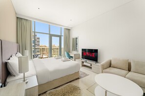 A modern hotel room with a large bed, a TV, a sofa, and a view of the city. - Modern Studio with Beach Access, Palm Jumeirah (Dubai)