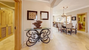 A spacious hallway with a dining area featuring a chandelier, framed artwork, and a decorative fish sculpture on a glass table.