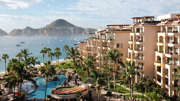 A resort with multiple-story buildings, a swimming pool, and a view of the sea with boats.