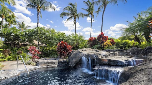 Un resort tropical con una piscina natural, cascadas y abundante vegetación.