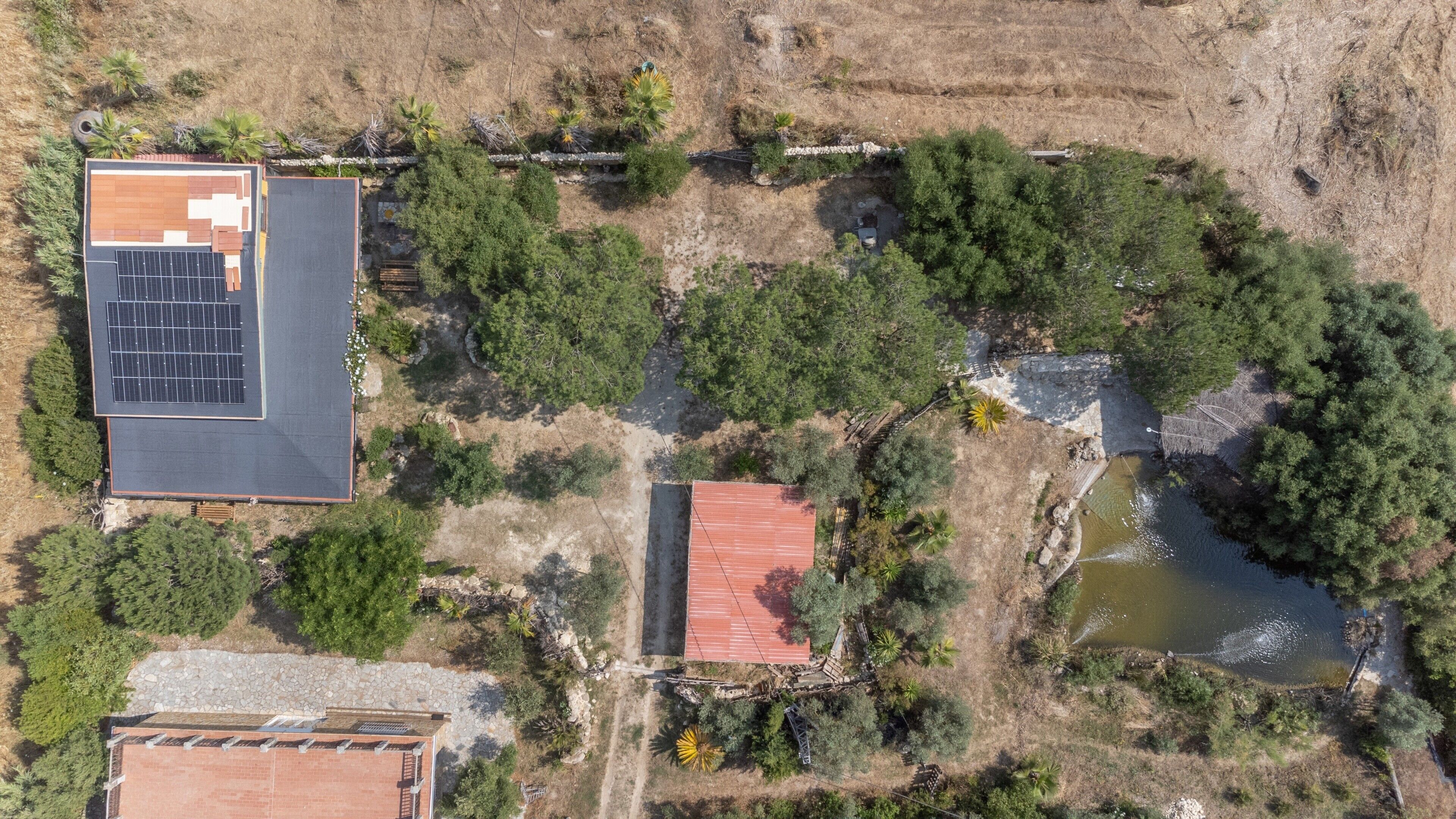 An aerial view of a property with a solar panel array, a red-roofed building, and a pond.
