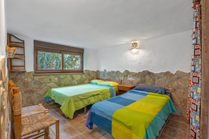 A bedroom with two beds, a window, a stone wall, and a small nightstand.