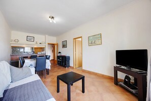 Ett hotellrum med en säng, ett litet bord, en TV, en liten köksdel och ett matbord.