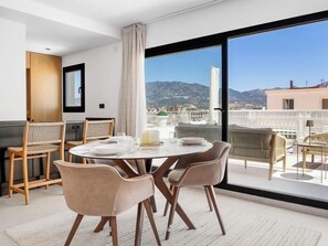 A modern dining area with a round table, chairs, and a view of the cityscape through large windows. - Las Cuevas | Beachfront - Sea View - Terrace (Fuengirola)