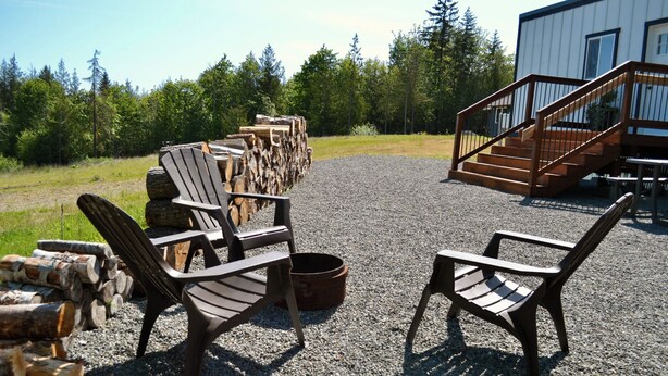 Une terrasse en gravier avec des fauteuils Adirondack, un foyer et une pile de bois de chauffage.