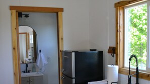 Une cuisine compacte avec des meubles en bois, un réfrigérateur en acier inoxydable, un évier et une fenêtre donnant sur un espace verdoyant.