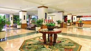 A spacious lobby with a central round table, multiple seating areas, and potted plants.