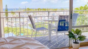 A bedroom with a large bed, a balcony with a view of the marina, and a potted plant.