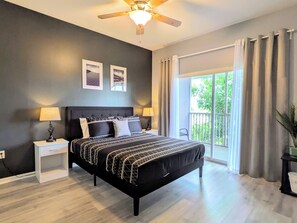 A modern bedroom with a large bed, two bedside tables, a ceiling fan, and a balcony with curtains.