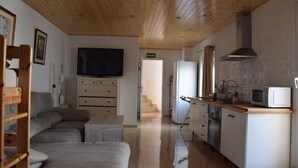 Una cocina compacta con electrodomésticos blancos, techo de madera y un sofá en la zona de estar.