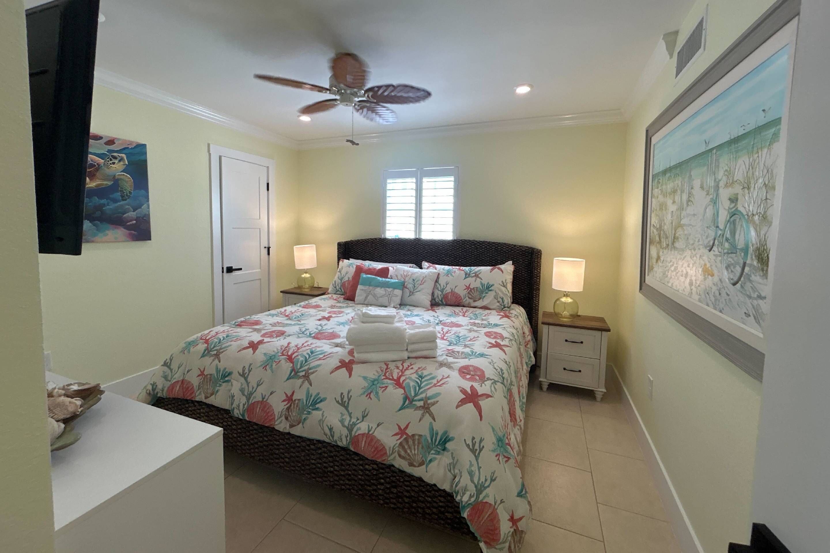 A bedroom with a bed, bedside lamps, a ceiling fan, and artwork on the walls.