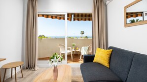 A modern living room with a grey sofa, a wooden coffee table, and a view of the beach through large glass doors.