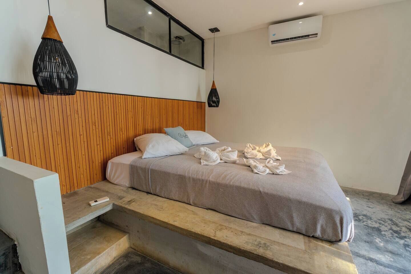 Een moderne slaapkamer met een houten hoofdbord, een bed met wit en grijs beddengoed en een paar handdoeken op het bed.