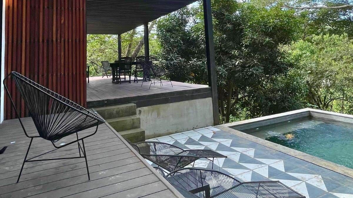 A covered outdoor area with a pool, wooden deck, and metal chairs.