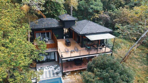 Une maison moderne dotée d’une grande terrasse, d’une piscine et d’un espace de détente extérieur abrité, le tout entouré d’une végétation luxuriante.