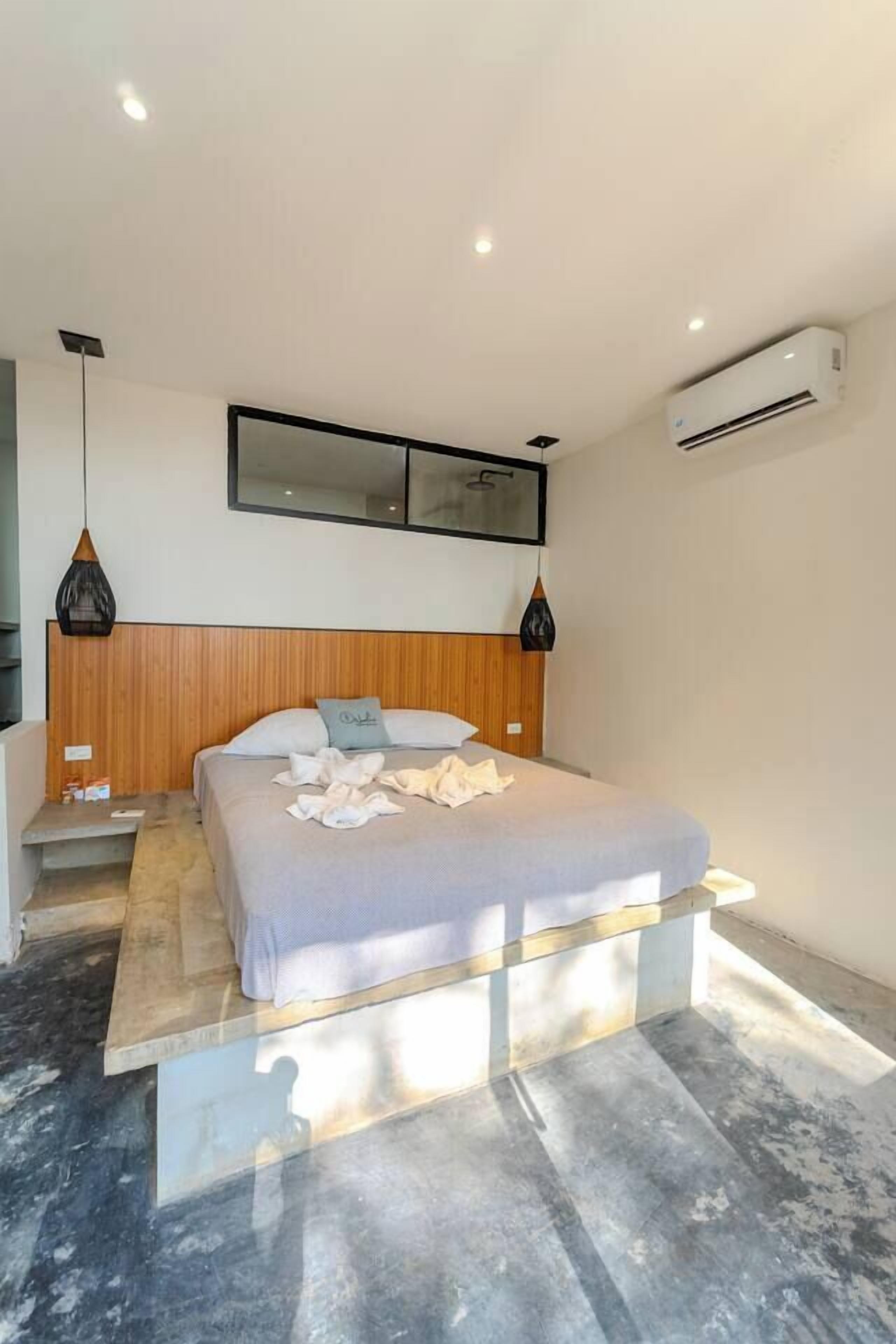 Een moderne slaapkamer met een bed, nachtkastjes, een houten hoofdbord, een airconditioner en hanglampen.