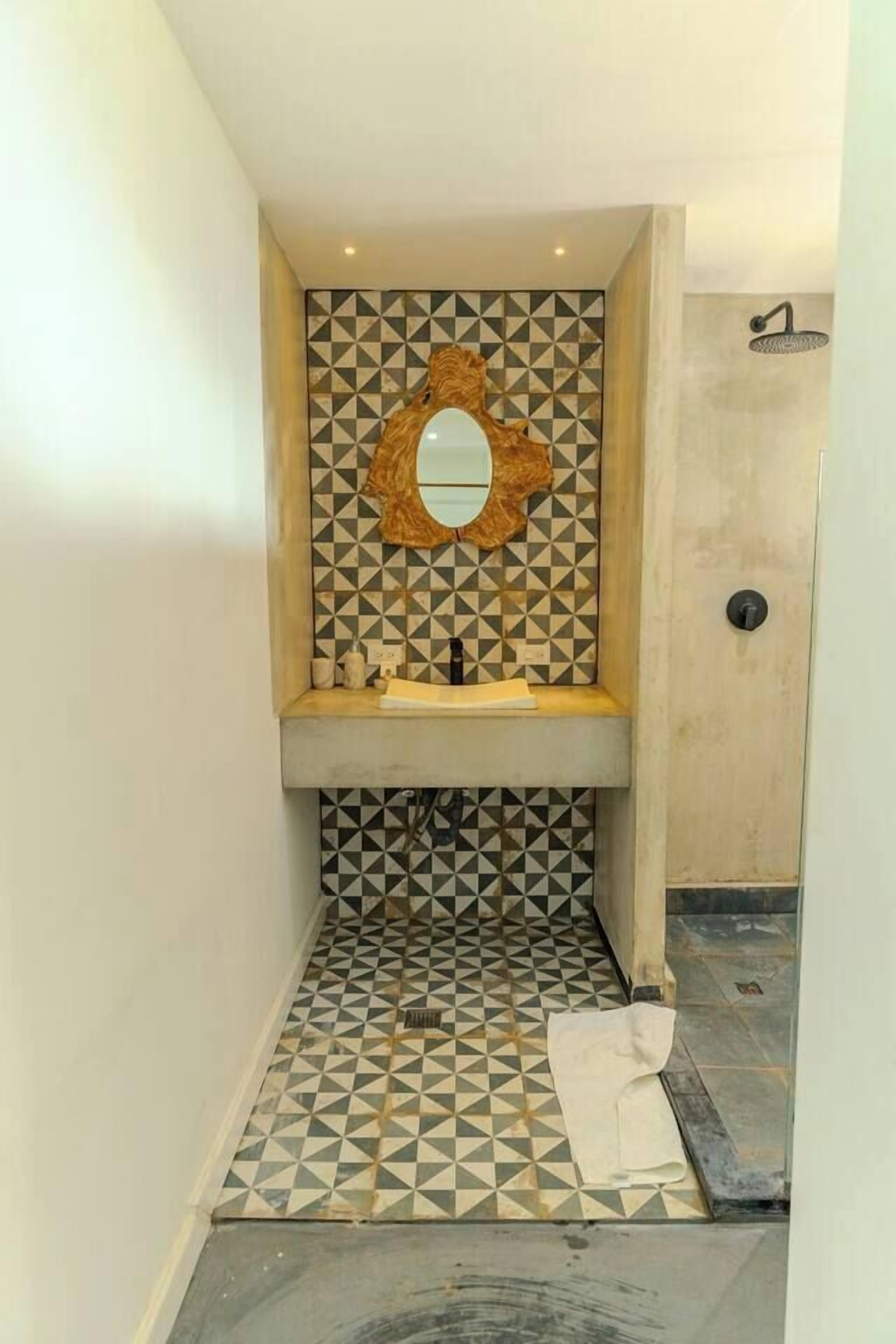 A bathroom with a geometric patterned tile floor, a sink with a mirror above it, and a shower area.