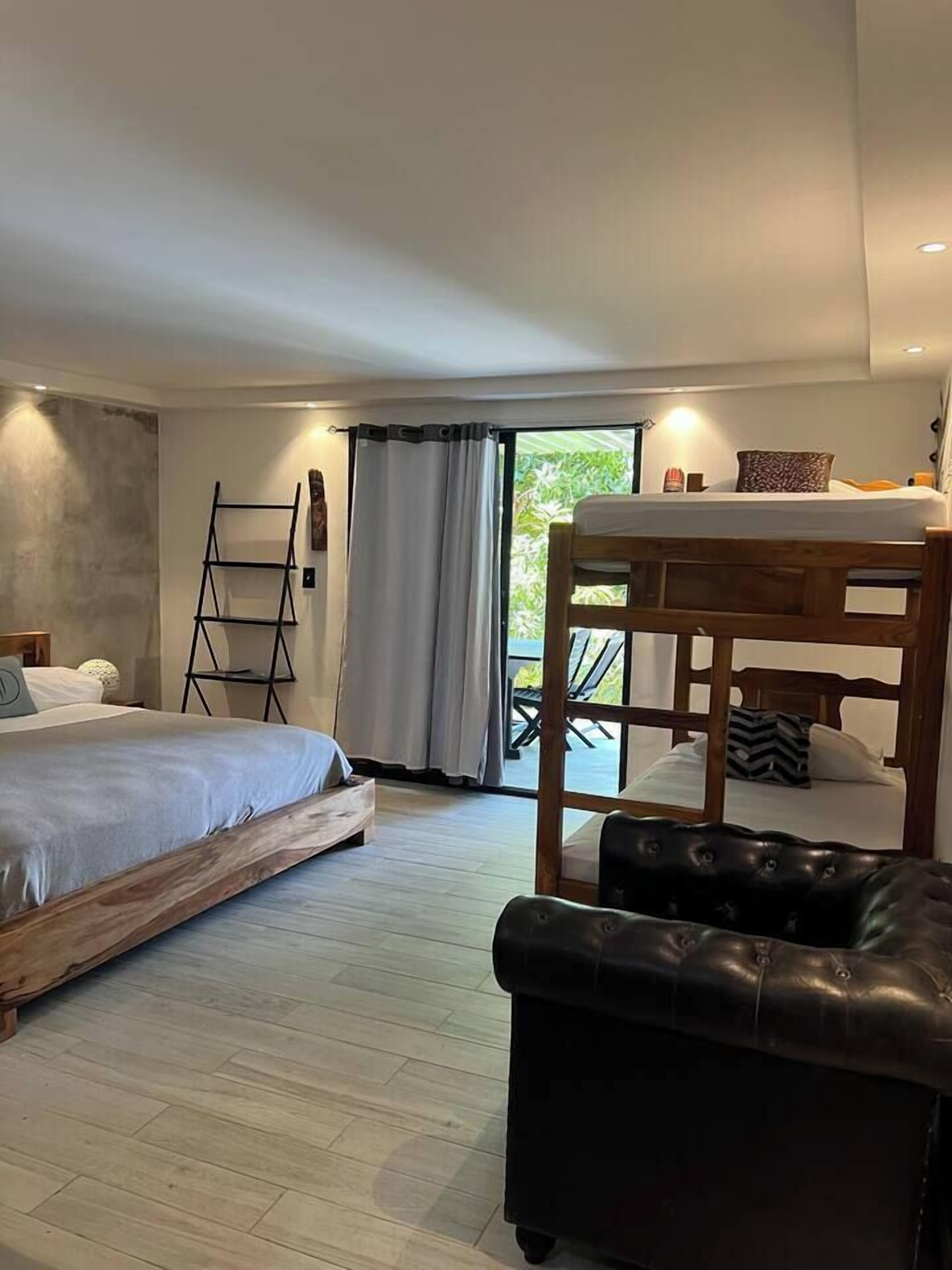Ein Schlafzimmer mit einem Bett, einer Holzbank, einem schwarzen Lederhocker und einer an der Wand stehenden Leiter.