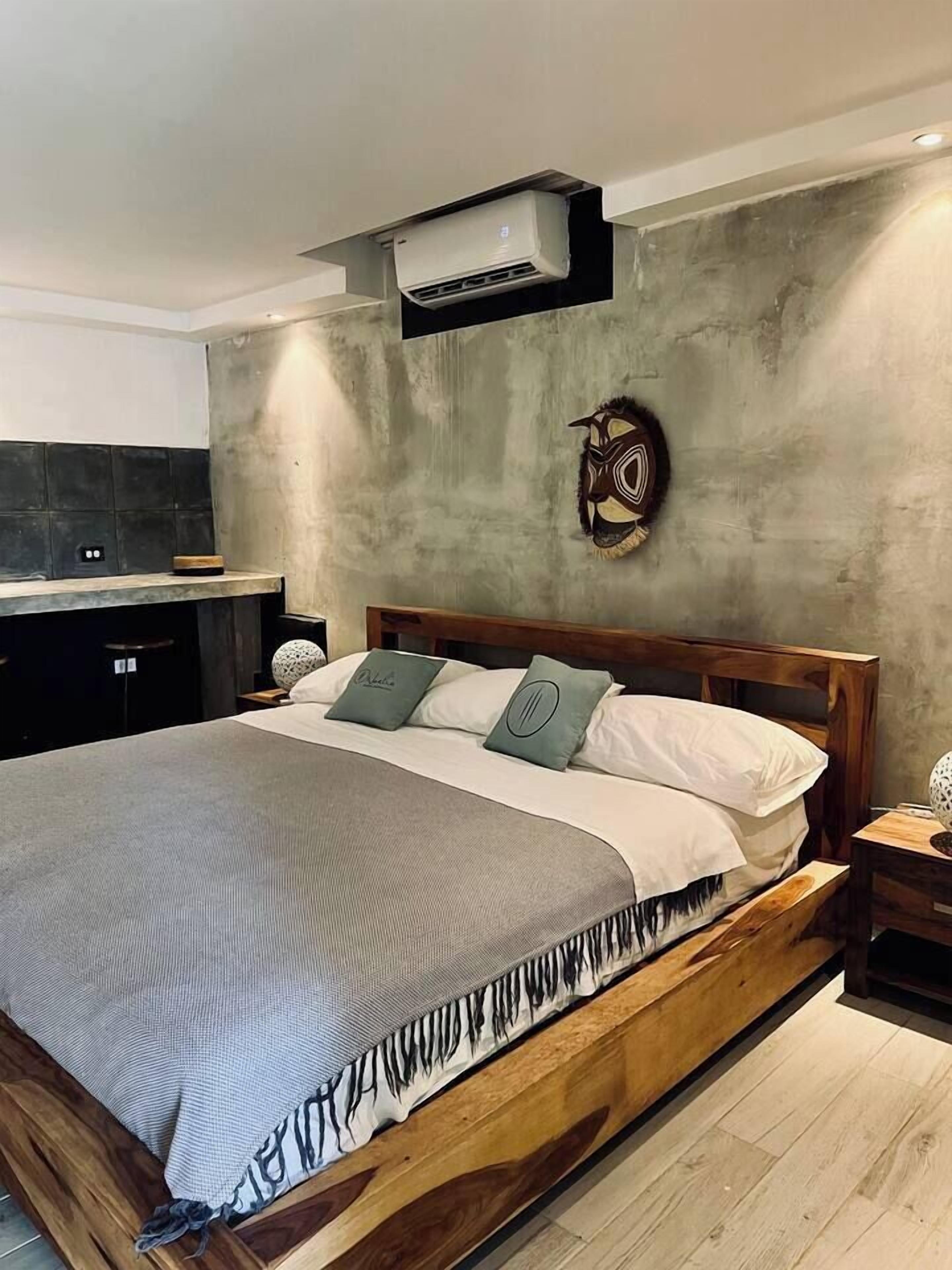 A modern bedroom with a wooden bed, a concrete accent wall, and a built-in air conditioning unit.