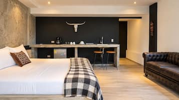 Un dormitorio moderno con una cama grande, una kitchenette pequeña y un sofá de cuero.