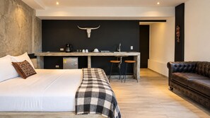 A modern bedroom with a large bed, a small kitchenette, and a leather sofa.