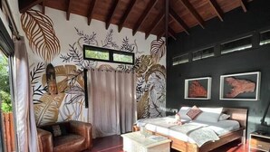 Une chambre avec un plafond en bois, un lit, une table de chevet, un canapé et un mur orné de motifs de feuilles.