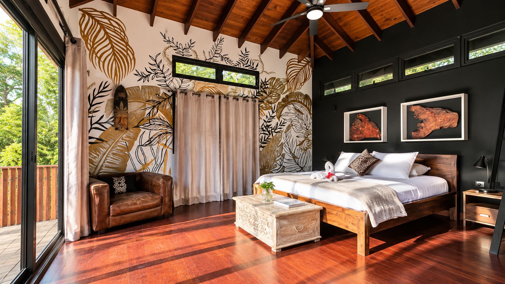 Un dormitorio con una cama grande, techo de madera, vista por una ventana y una pared con diseños de hojas.