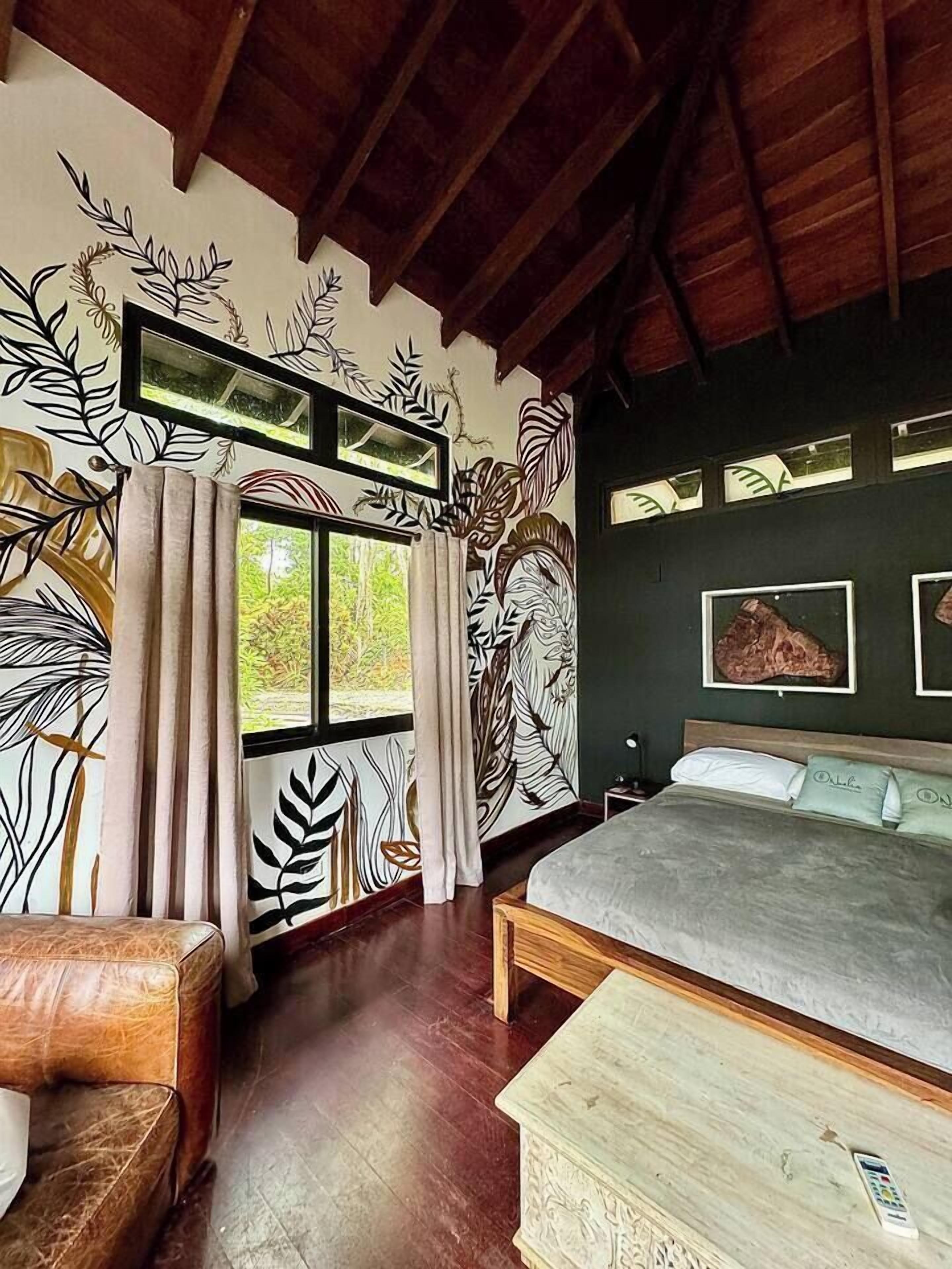 Un dormitorio con cama, cabecera de madera, mesita de noche, silla y ventana con cortinas.