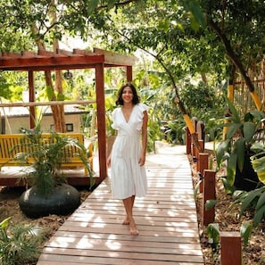 A wooden pathway in a lush garden with a wooden pergola and yellow chairs.