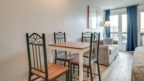 Een kamer met een houten tafel en vier stoelen, een bed, een bank en een balkon met blauwe gordijnen.