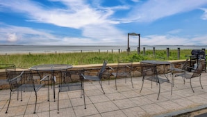 Een terras buiten met metalen stoelen en tafels, met uitzicht op een strand en de oceaan.