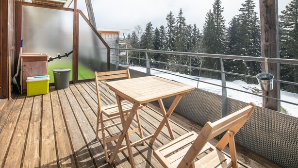 Une terrasse en bois avec une table et des chaises, donnant sur un paysage enneigé parsemé d’arbres.