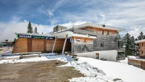 Un bâtiment moderne à plusieurs étages, doté d’une façade en bois, d’un balcon et d’un télésiège visible au loin.