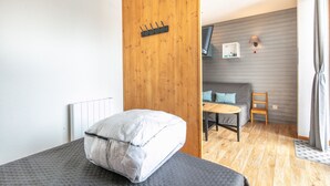 Une chambre avec un lit, une cloison en bois, une petite table avec une chaise et un téléviseur fixé au mur.