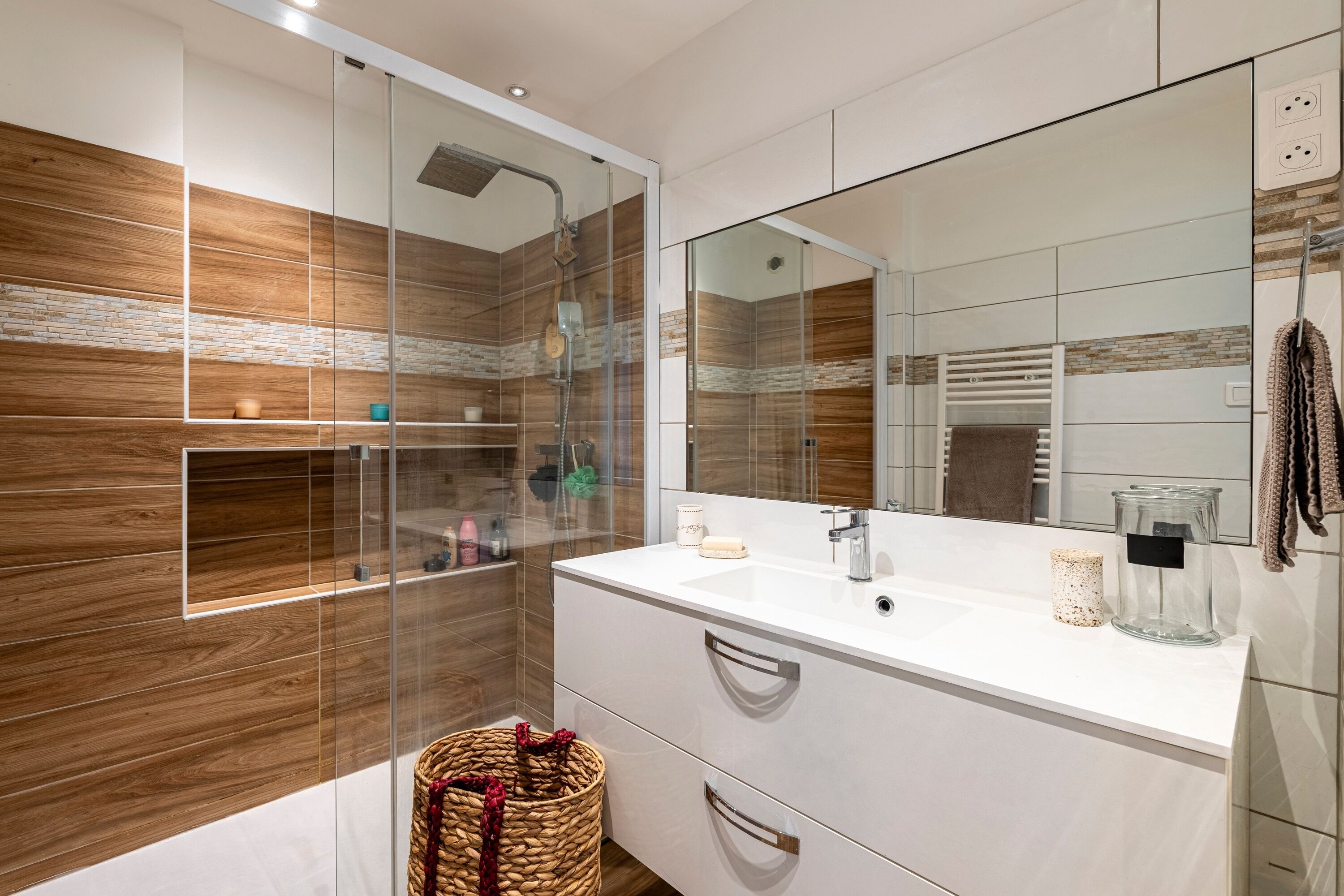 A modern bathroom with a glass-enclosed shower, a large mirror, and a white vanity.