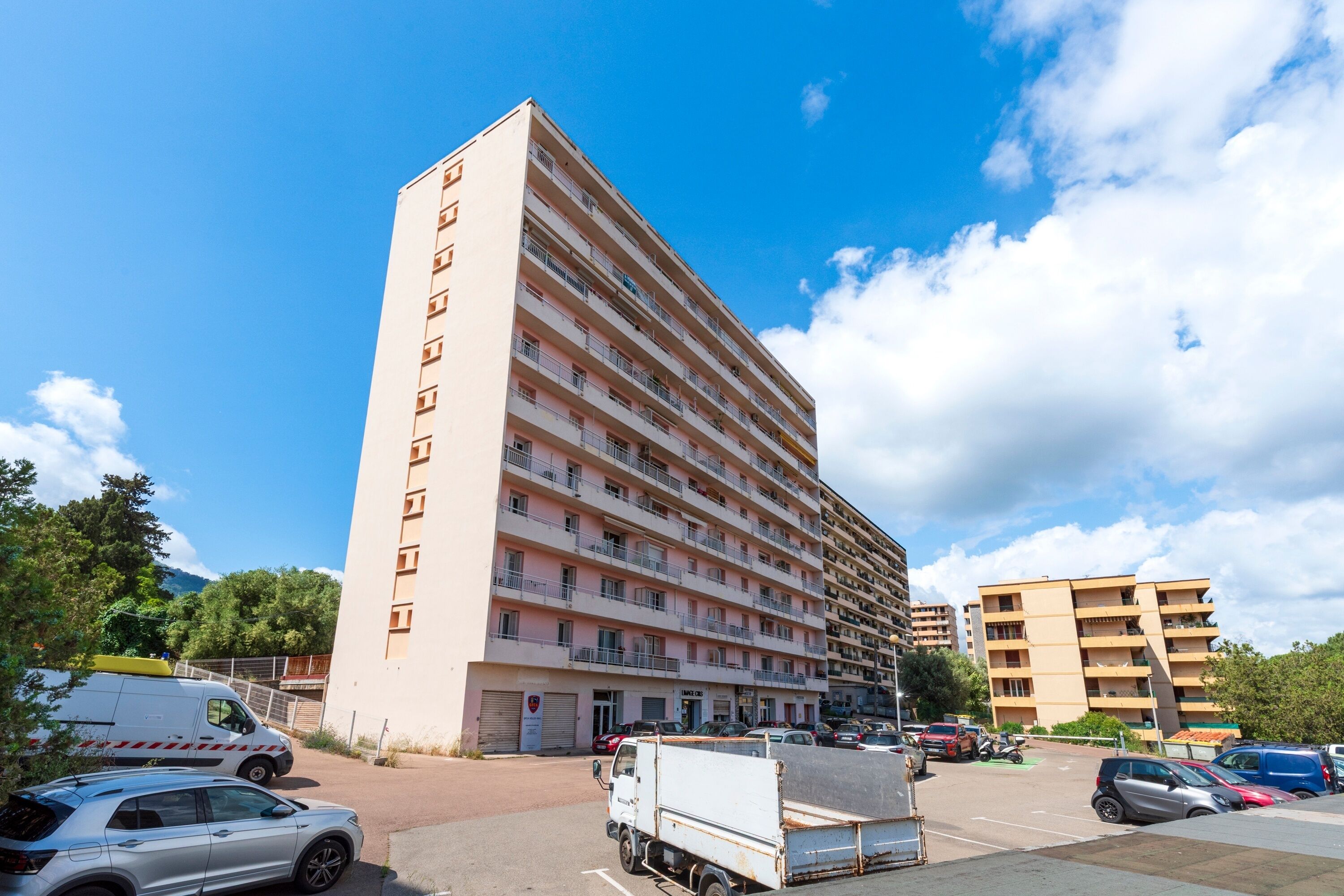 Hotel de diverses plantes amb façana plana, balcons i un pàrquing amb diversos vehicles.
