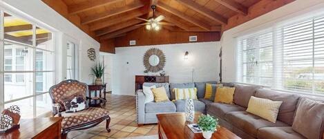 A spacious living room with wooden beams, a sofa set, a coffee table, and a decorative mirror.