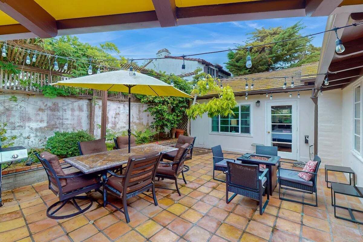 An outdoor patio with a table and chairs, surrounded by a stone floor and covered by a yellow umbrella.