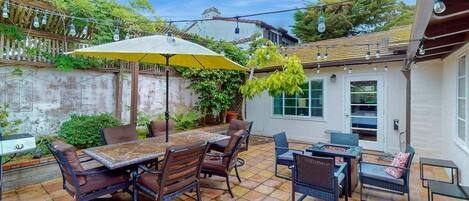 An outdoor patio with a table and chairs, surrounded by a stone floor and covered by a yellow umbrella.